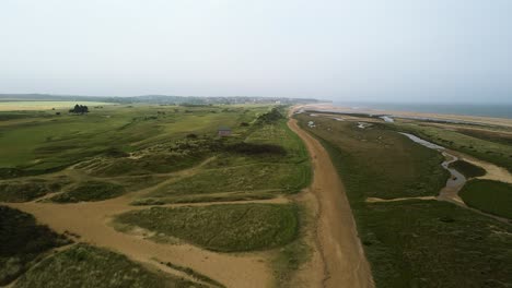 Ascending-drone-aerial-shot-of-Norfolk-coast-with-Golf-course,-marsh-land,-sand-dunes-and-sea-in-view-looking-out-to-Hunstanton-in-the-distance