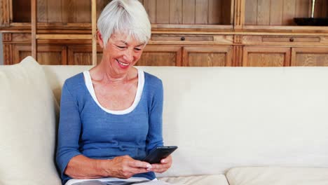 mujer mayor usando teléfono móvil en la sala de estar