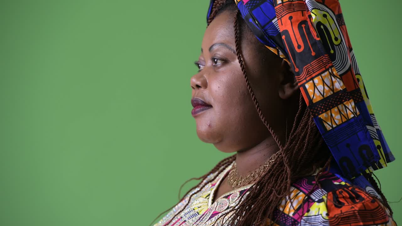 Overweight beautiful African woman wearing traditional clothing against green background