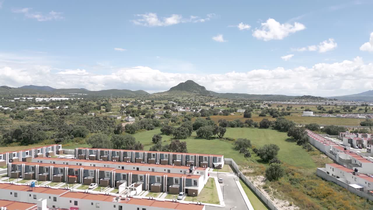 Backward Drone Aerial Pullback Revealing Urban Sprawl Emerging From Rural Landscape With Hills on the Horizon in Mexico – Sunny 4K