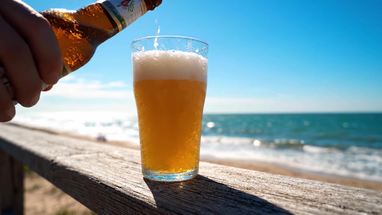 Momenti rinfrescanti al mare: un bicchiere di birra frizzante attende mentre le onde lambiscono dolcemente la riva sotto un glorioso cielo blu.