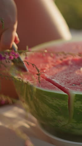 primer plano de una mano sosteniendo firmemente una jugosa sandía roja mientras corta a través de su carne vibrante, la cáscara fresca y verde contrasta con el interior rosado mientras el individuo corta la fruta