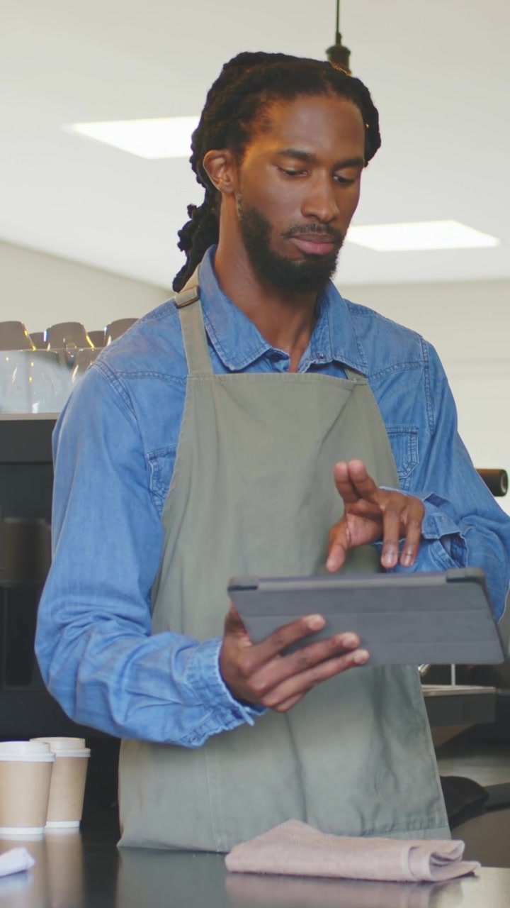 Vertical video: Hearing offscreen customer, barista in apron tapping tablet, taking orders, cups