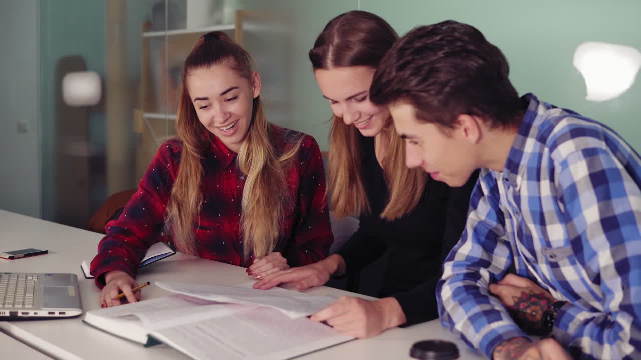 estudiantes felices trabajando en sus tareas sentados juntos en la mesa y bebiendo café. grupo de jóvenes en la reunión en un apartamento moderno. slowmotion tiro