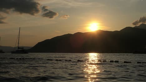 Magic-hour-at-sea,-sailing-boats-and-sun-setting-behind-mountain,-Mediterranean