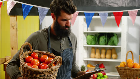 Personal-Masculino-Mirando-La-Lista-De-Verificación-Y-Sosteniendo-Una-Canasta-De-Tomates