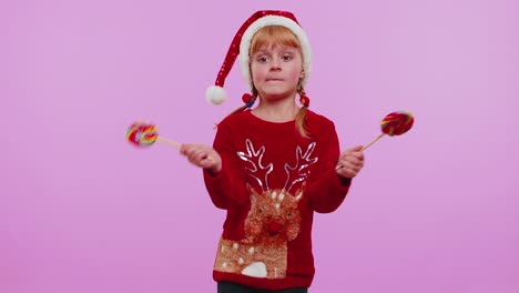 Joyful-girl-in-Christmas-sweater,-hat-holding-candy-striped-lollipops,-dancing,-making-silly-faces