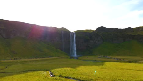 Rotation-around-the-Seljalandsfoss-waterfall-in-Iceland-in-spring,-with-the-flair-of-the-sun,-the-greenery
