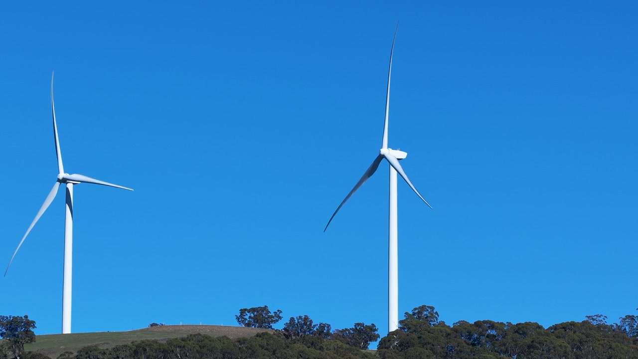 Due turbine eoliche in rotazione contro un cielo azzurro limpido.