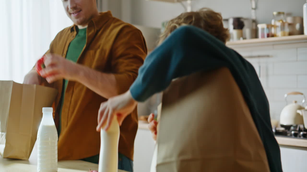 Família desempacotando sacolas de papel, retirando alimentos saudáveis em um apartamento claro, em primeiro plano.