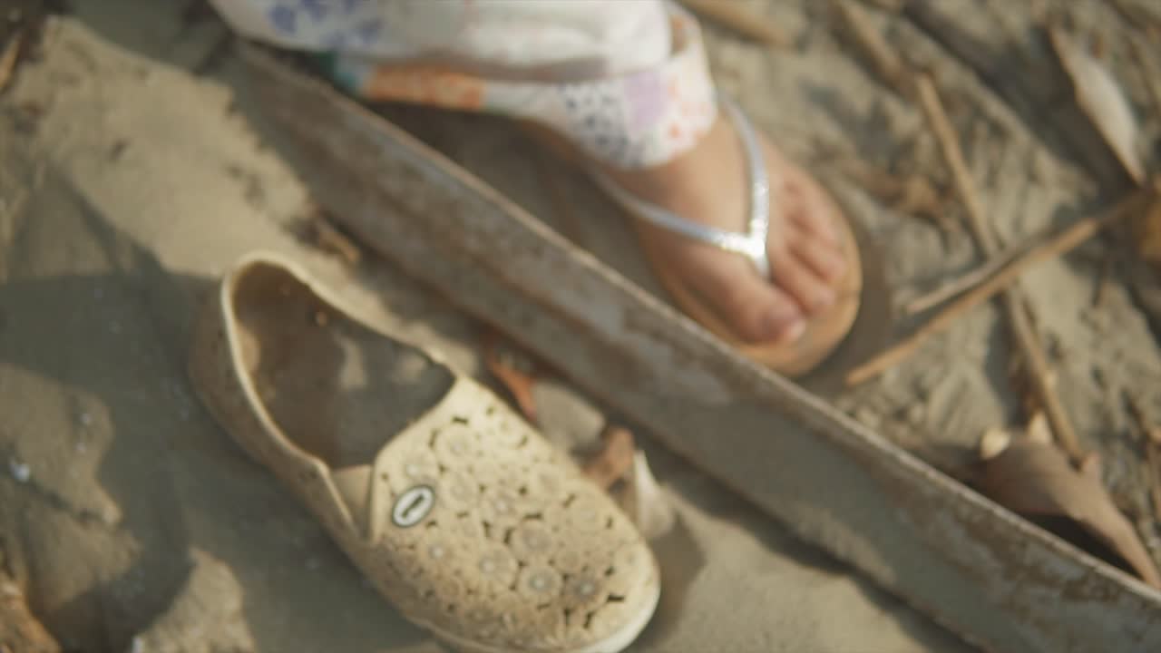 toma cinematográfica de una modelo de moda india caminando con sandalias al lado de un zapato viejo en una playa de arena en goa, india