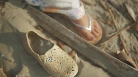 cinematic shot of an indian fashion model stepping with sandals next to an old shoe on a sandy beach in goa india