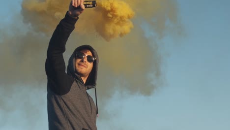 slow motion footage of a mysterious protester man with a hood on holding a yellow colored smoke grenade in the outside