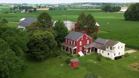 Orbit-of-red-farmhouse-and-farm-buildings-set-among-rural-fields-in-USA