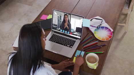 african american woman writing on memo notes having a video call on laptop at home