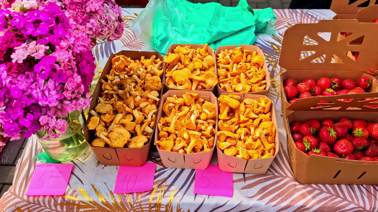 Baskets of fresh chanterelle mushrooms and strawberries at outdoor market stall
