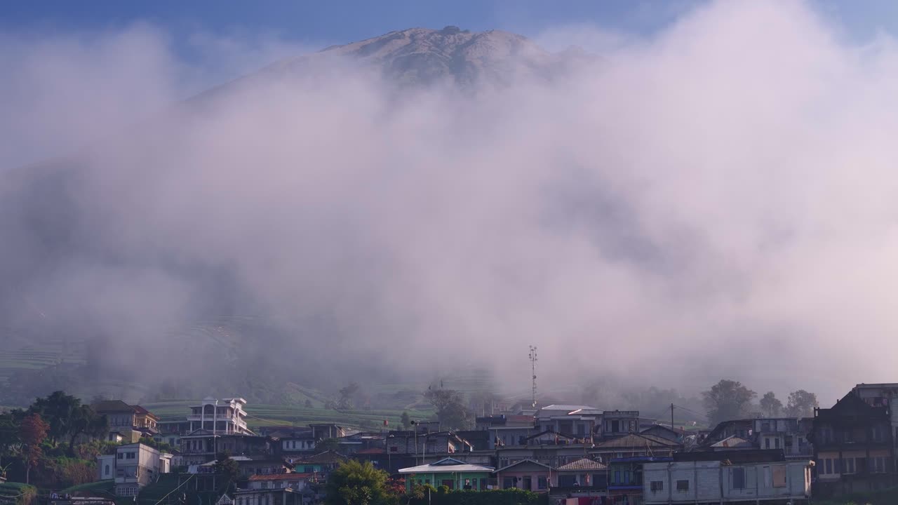 Scenic view of a mountain peak partially hidden by thick morning fog above a rural village