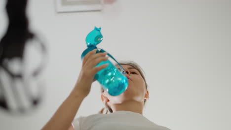mujer bebe agua corriendo en la cinta de correr en el gimnasio. mujer activa se refresca con agua clara haciendo ejercicio en el entrenador en el club bajo ángulo de tiro. rutina de entrenamiento