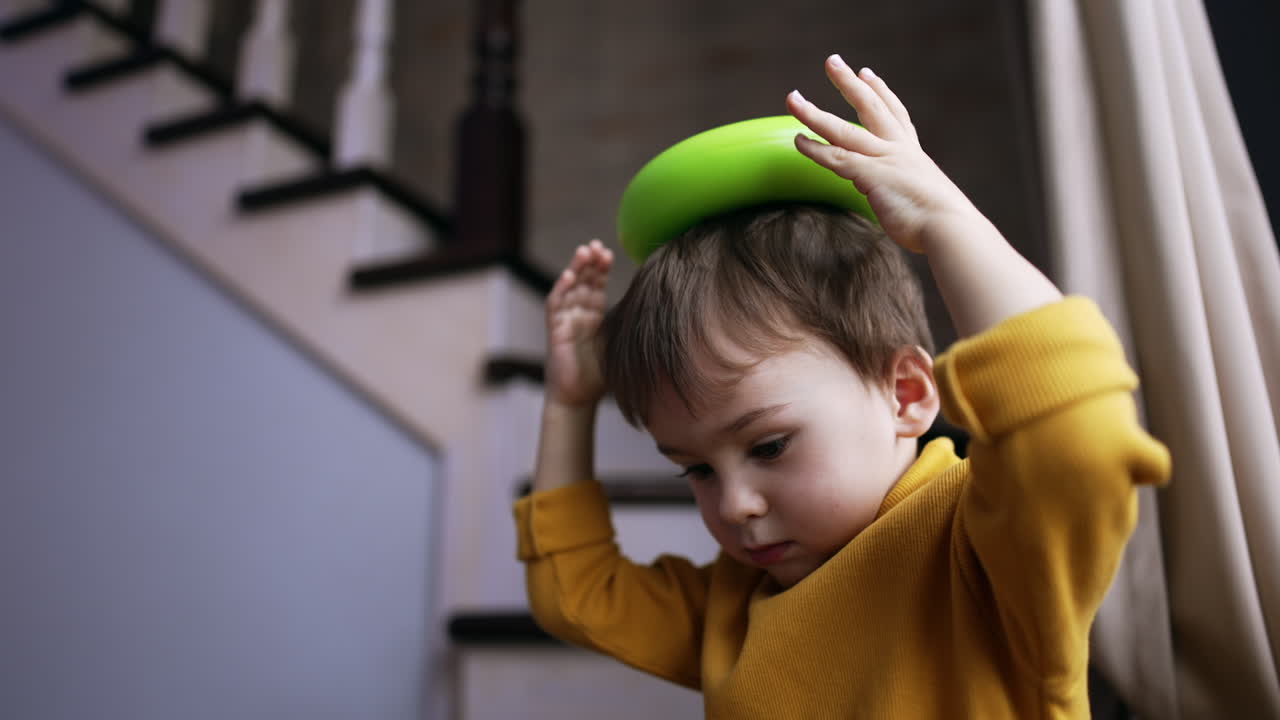 Lovely Caucasian baby boy playing at home. Toddler kid puts the toy on his head. Close up.