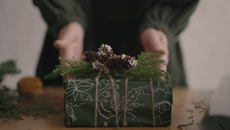 la cámara sigue el regalo. una mujer con sus manos empuja una caja de navidad con decoraciones en la cámara. hermoso regalo de navidad hecho con sus propias manos de materiales ecológicos