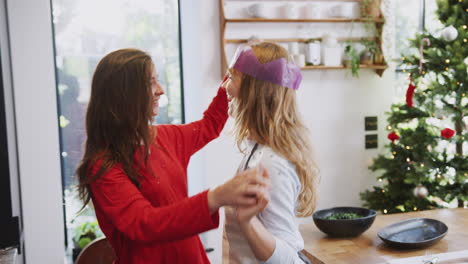 gay female couple at home dancing in kitchen as they prepare dinner on christmas day together