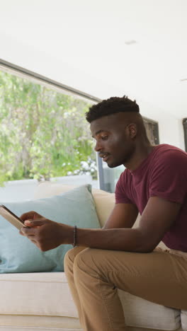video vertical de un hombre afroamericano feliz usando una tableta en casa