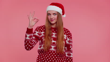 Adult-girl-in-Christmas-sweater-looking-approvingly-at-camera-showing-ok-gesture,-like-sign-positive