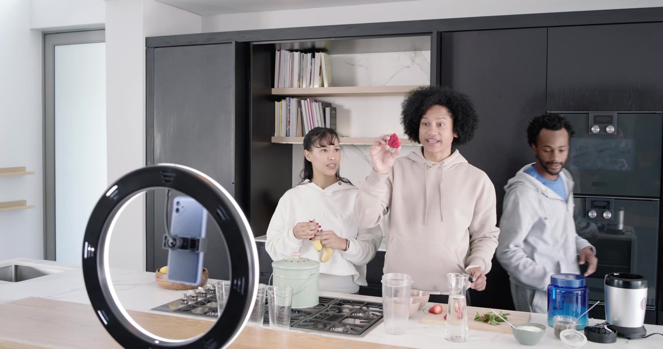 Amici di diverse etnie che prendono una banana, preparano sull'isola della cucina e filmano un frullato con una ring light.