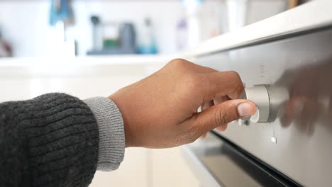 close-up of a person turning a knob on an oven