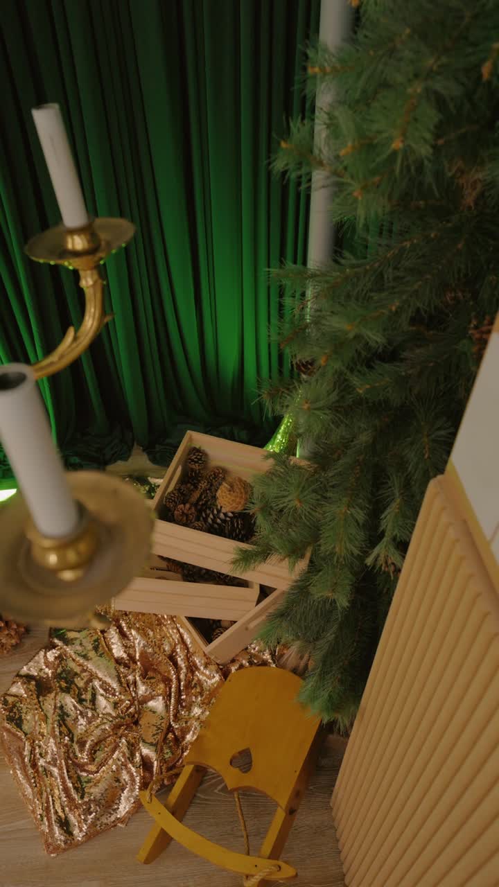una cálida viñeta navideña con un candelabro dorado, cajas apiladas de piñas y exuberantes toques de hoja perenne contra ricas cortinas verdes.