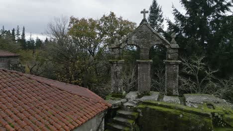 Aerial-drone-shot-of-an-old-monastery-construction-surrounded-by-trees-and-nature-with-a-Christian-cross-on-top-and-red-roofs