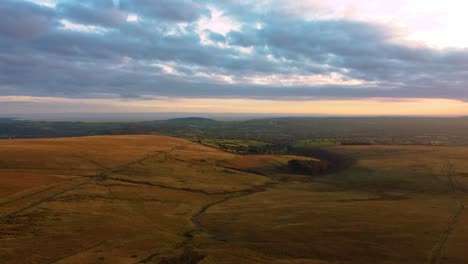 Wide Landscape Aerial View of Open Moorland in Wales with Long Country Road with Paths and Tracks Carving Through the Terrain with Blue Tinted Clouds near Swansea 4K
