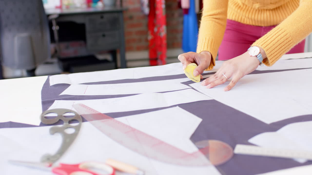 Biracial female fashion designer using pattern and marking cloth with chalk on table, slow motion