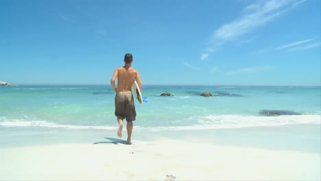 man running to the edge of water with his surf board