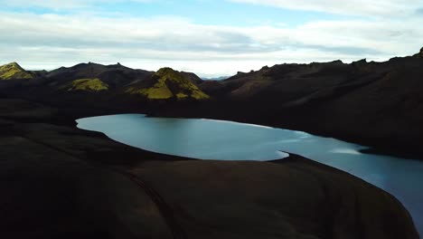 Aerial-landscape-view-of-a-turquoise-volcanic-lake-in-the-Icelandic-highlands-dark-mountains,-on-a-cloudy-day