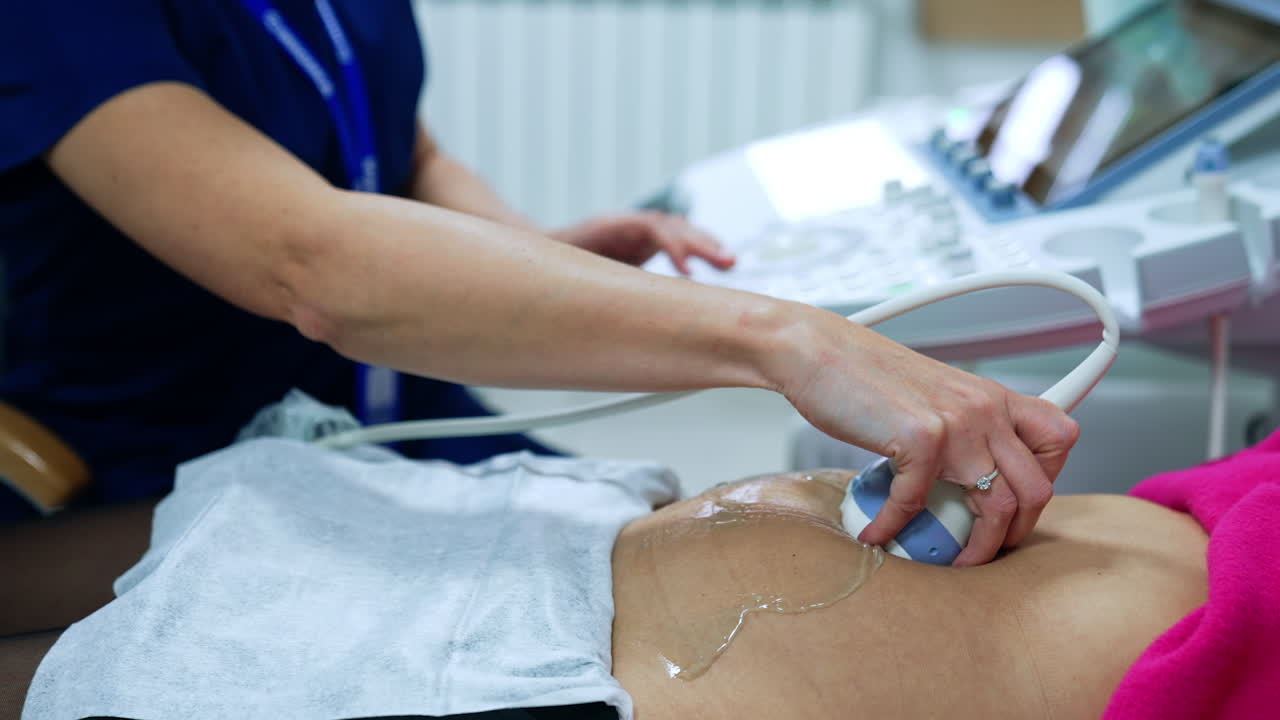 Pregnant patient is checked on the ultrasonic equipment. Obstetrician's hand moving transducer by the belly of female. Close up.