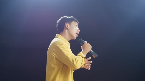 side view of young asian boy holding a microphone and rapping on the black background