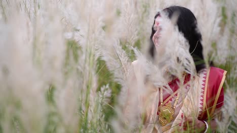 Eine-Glückliche-Und-Verspielte-Verheiratete-Indische-Bengalische-Frau,-Die-Saree-Trägt,-Spielt-Mit-Dem-Langen-Weißen-Gras-Auf-Einem-Feld-Für-Durga-Puja-Oder-Poyla-Boisakh,-Zeitlupe