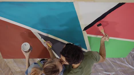 una joven pareja pinta en un lienzo dibujando una imagen en un estudio de arte y besándose, vista de ángulo alto