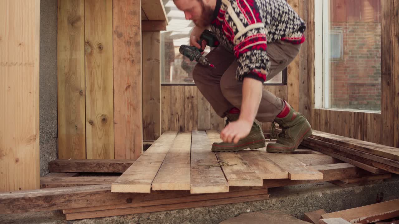 retrato de un hombre práctico instalando pisos de tabla de madera usando un destornillador sin cables
