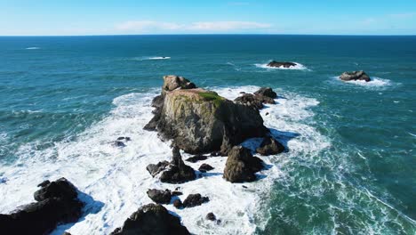 Hermosa-Toma-Aérea-De-Dron-De-4k-De-Olas-Oceánicas-Chocando-Contra-Rocas-En-Bandon,-Oregon-Con-Cielo-Azul-Amapola-En-El-Fondo