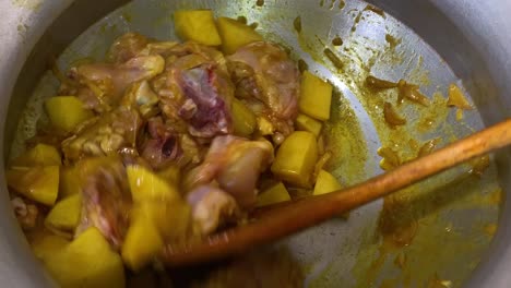 chicken and potato being mixed in large pot with wooden spatula