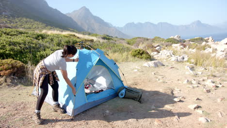 setting up blue tent, woman preparing campsite during mountain hike