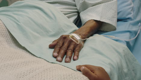 Niña-Tocando-La-Mano-Del-Abuelo-Acostado-En-La-Cama-Del-Hospital-Niño-Mostrando-Afecto-Al-Lado-De-La-Cama-Por-El-Abuelo-Recuperándose-De-Una-Enfermedad-Atención-Médica-Apoyo-Familiar