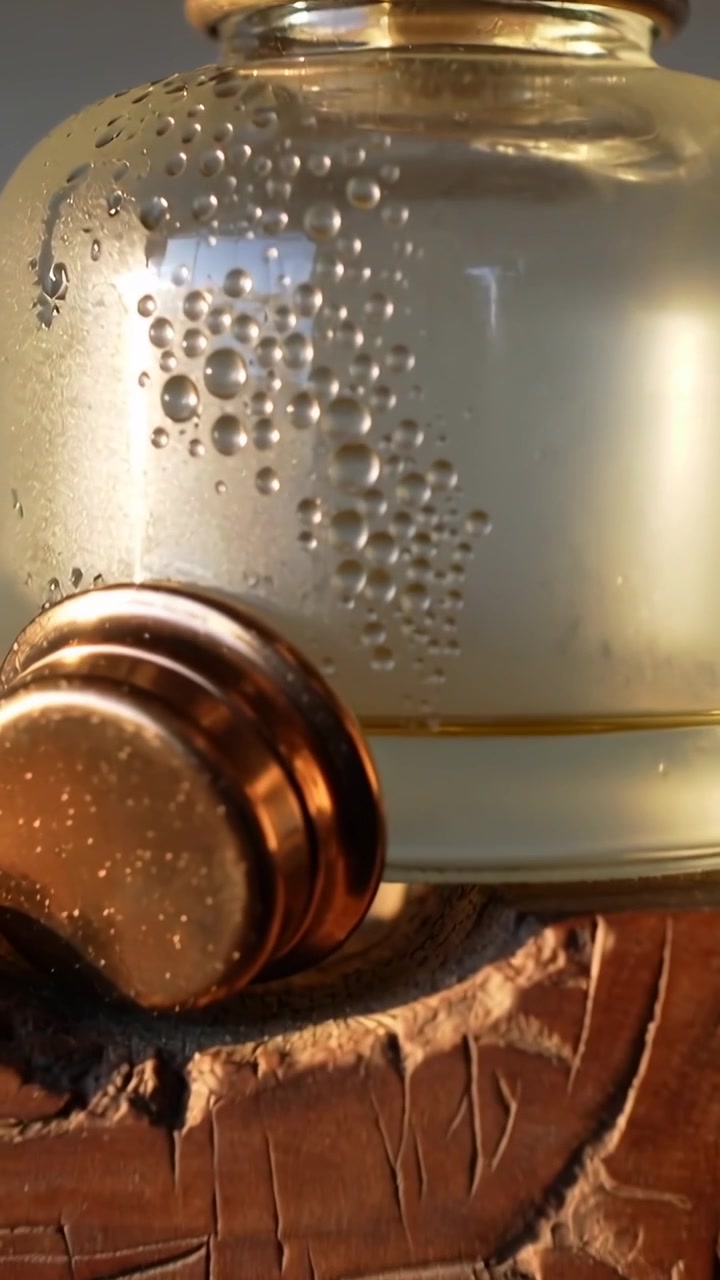 Vertical video: Moving camera revealing glass bottle on wooden base to show drops and copper ring