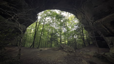 Female-hiker-walks-under-massive-natural-stone-arch-in-Tennessee-forest,-4K