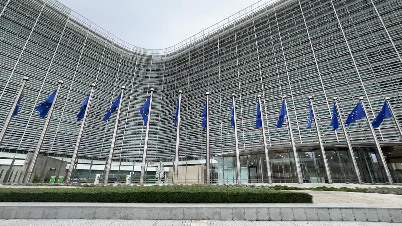 Inquadratura ampia dell'edificio della Commissione Europea a Bruxelles con bandiere dell'Unione Europea, che simboleggia politica, governance e istituzioni internazionali