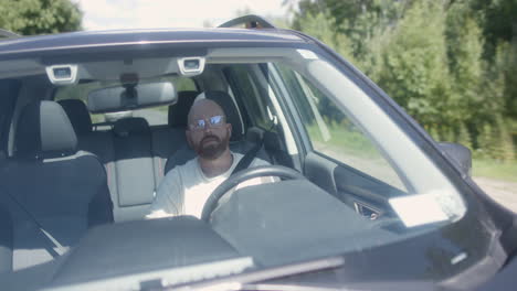 a bearded man with glasses drives on a rural road, turns left and pulls over