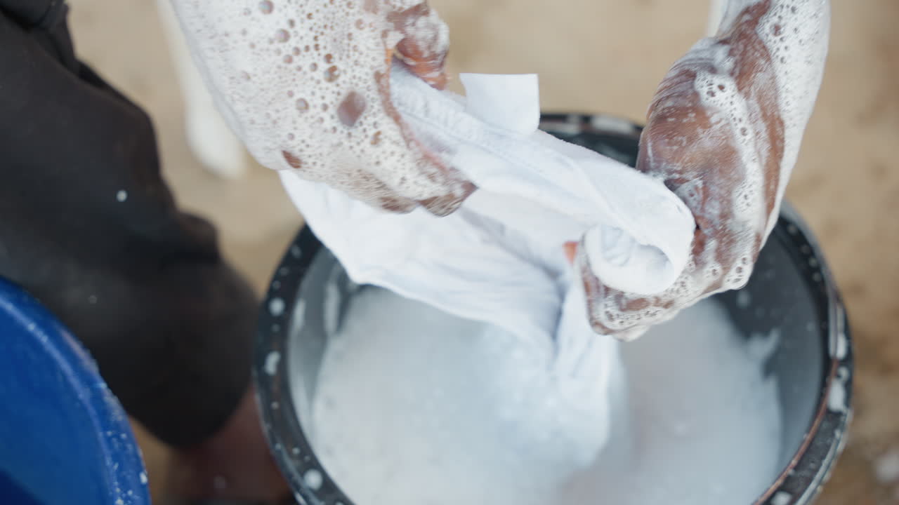 Strofinare una camicia con sapone. Processo di lavaggio a mano di una camicia bianca. Primo piano di mani che lavano i vestiti con sapone. Vista dettagliata del bucato manuale che include strofinatura e risciacquo con sapone.