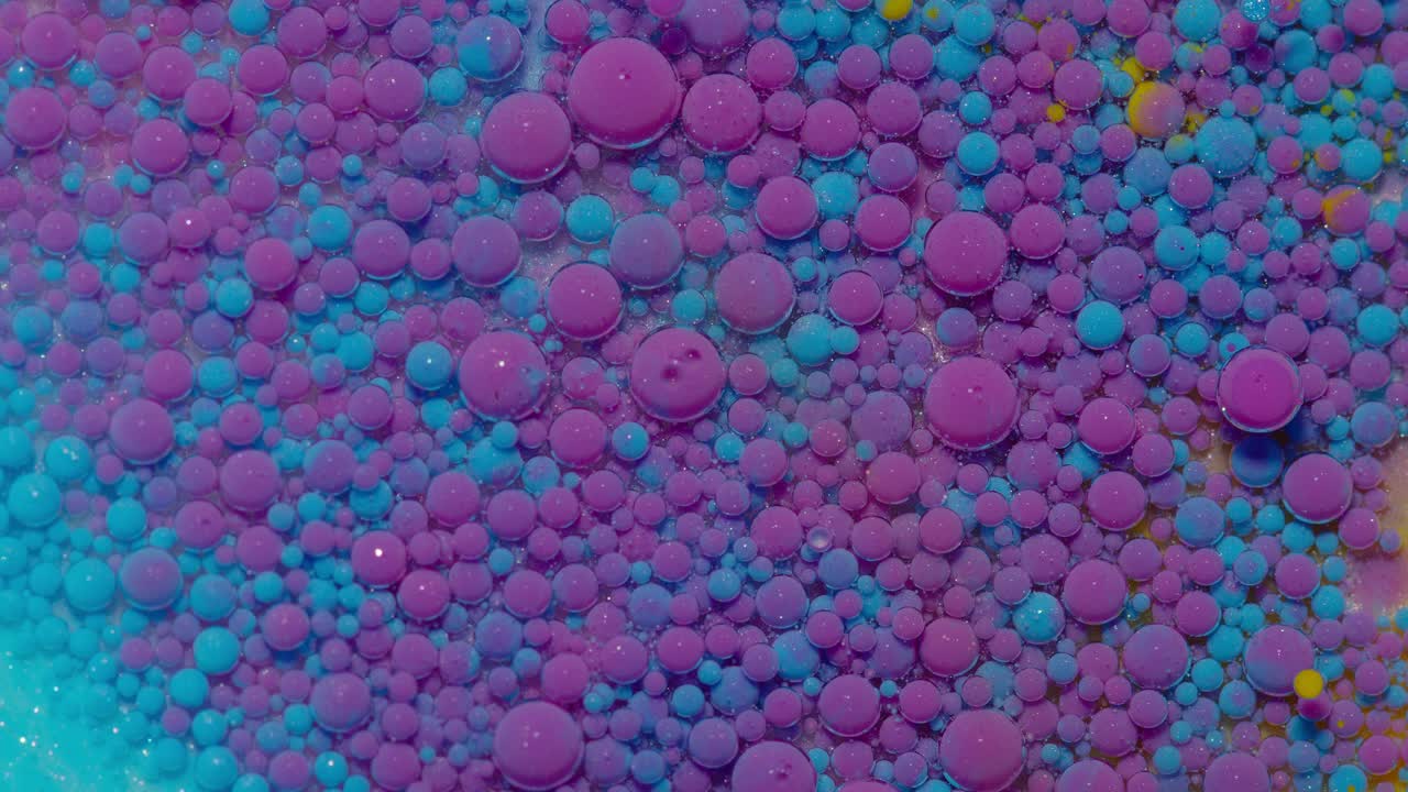 Ink bubbles mixed with liquid substance of oil, milk, soap, bright acrylic paint on colorful surface